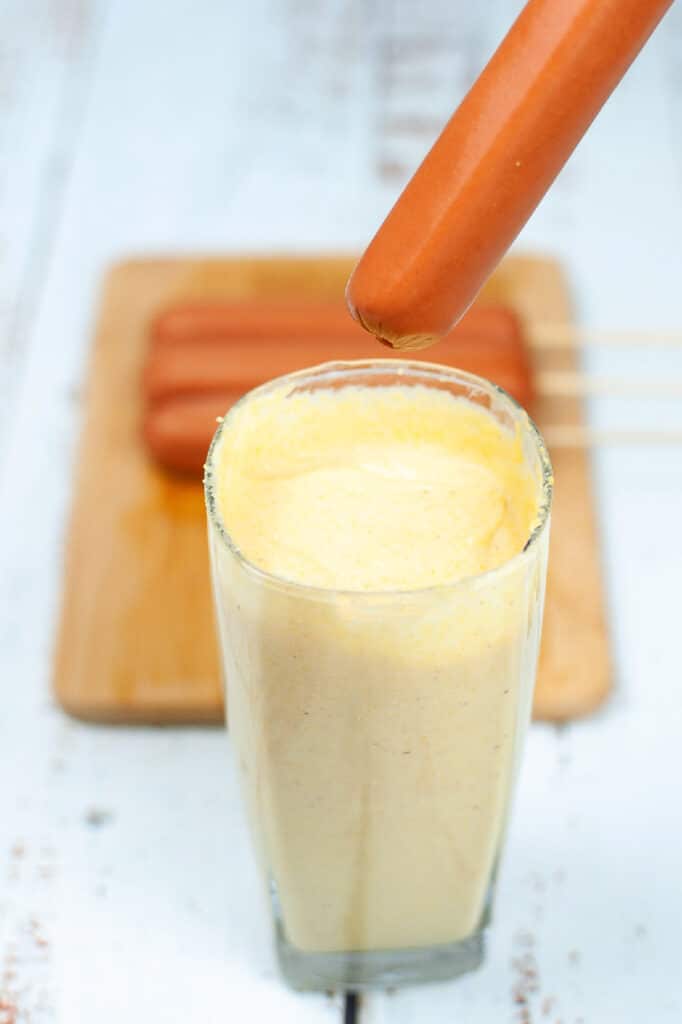 dipping hot dog in cornmeal batter for corn dogs