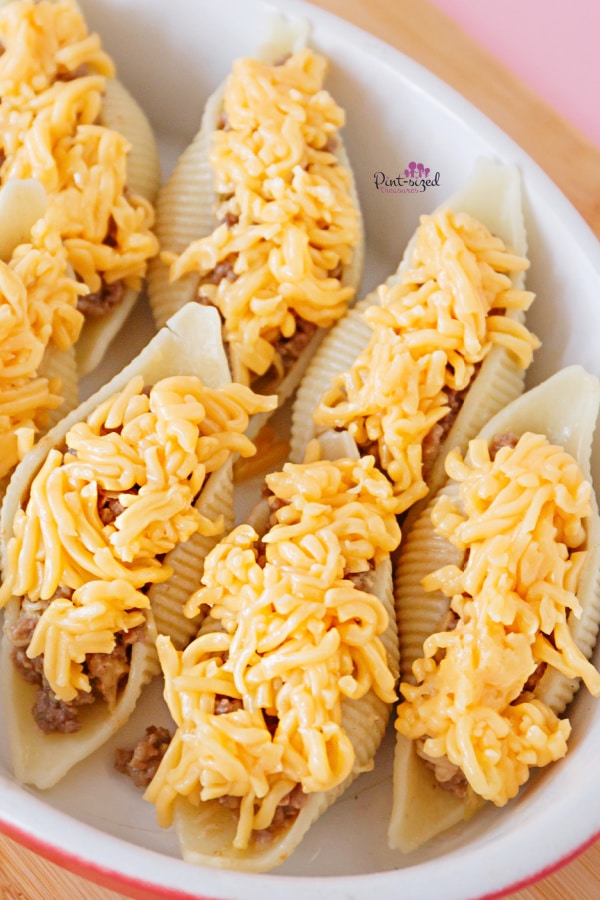 adding cheese to shells filled with cheeseburger mixture