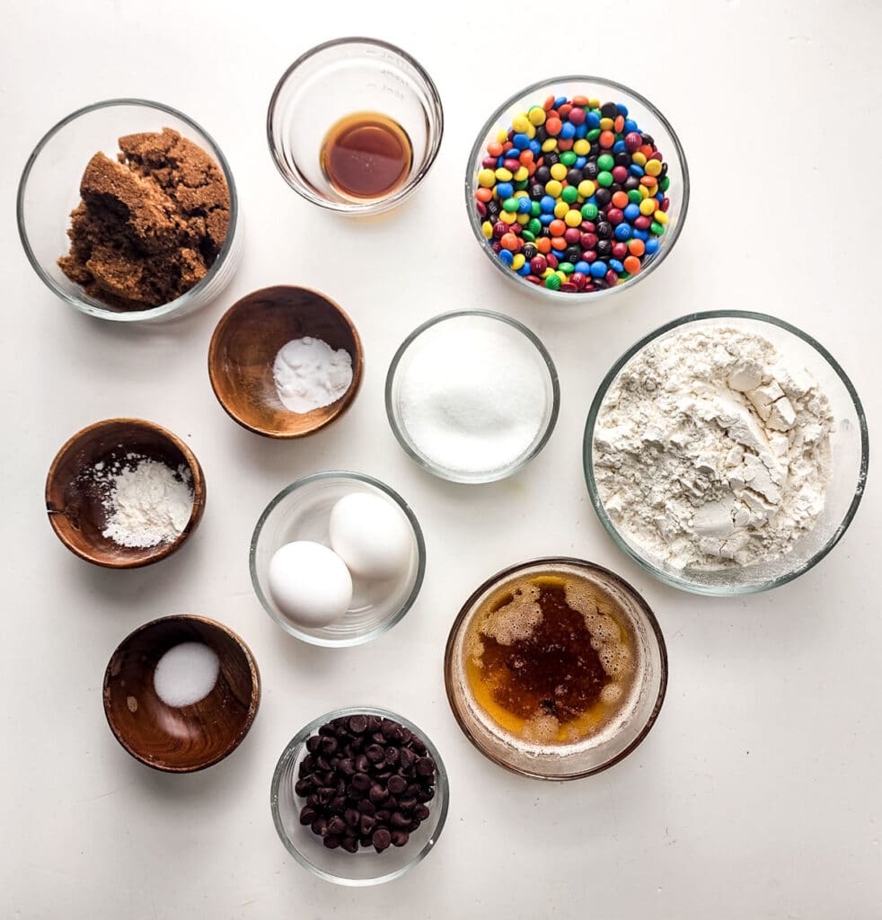 Ingredients for M&M cookie bars in bowls: flour, browned butter, sugars, eggs, mini M&M's